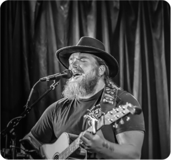 A man with a beard and hat playing guitar